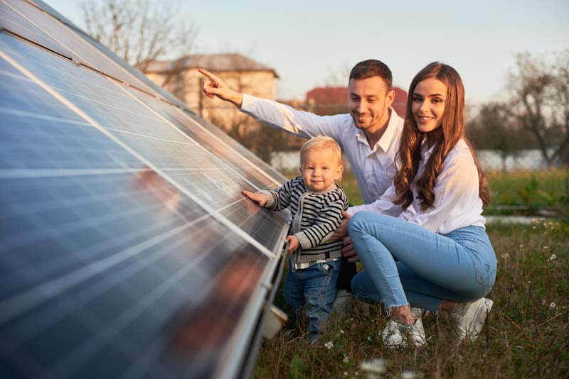 Young couple with toddler standing next to solar panels on ground